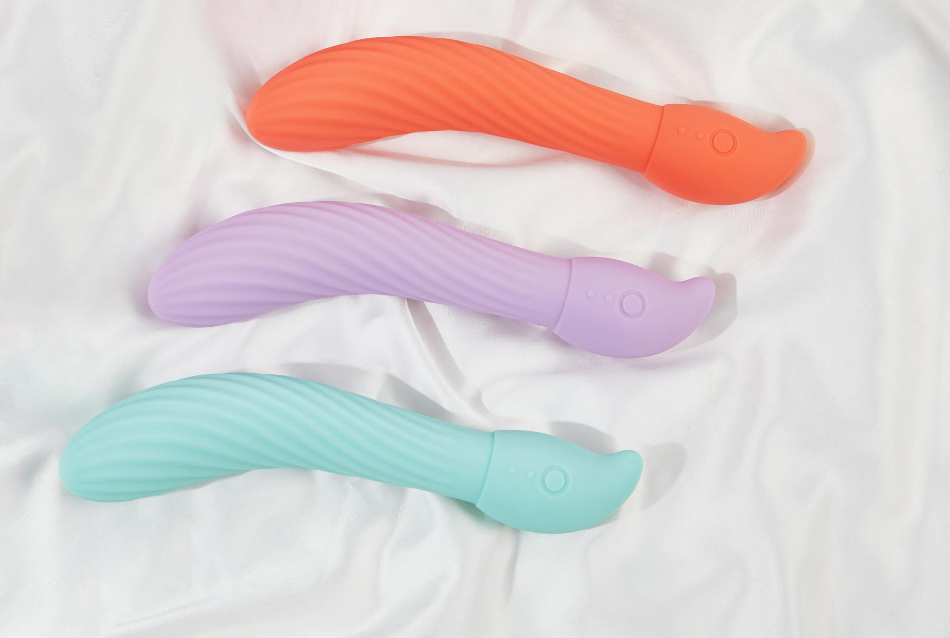 Three colorful vibrators arranged on white fabric, highlighting smooth texture and design variations.