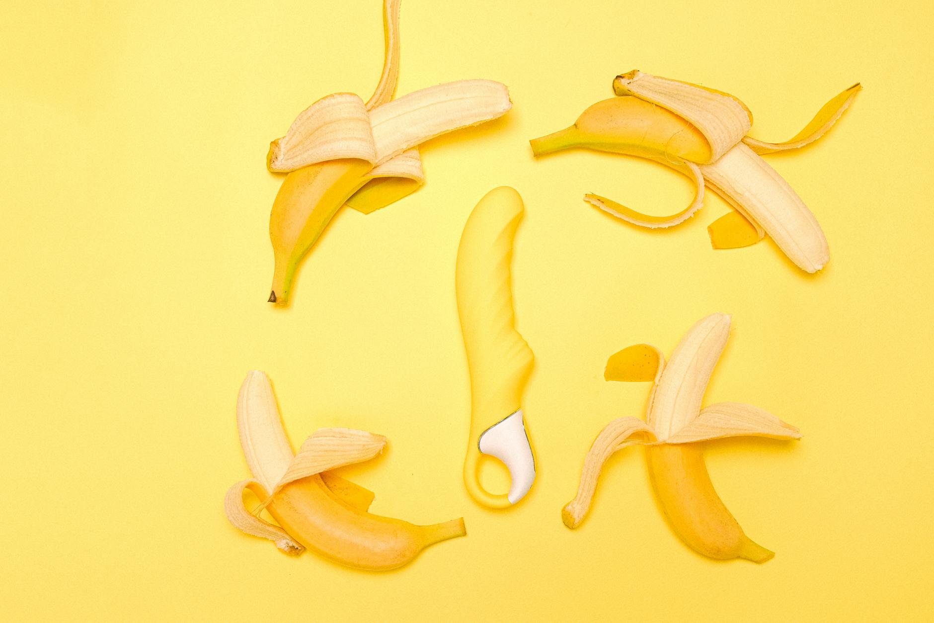Yellow silicone lemon vibrator surrounded by fresh lemons on a sunny yellow background