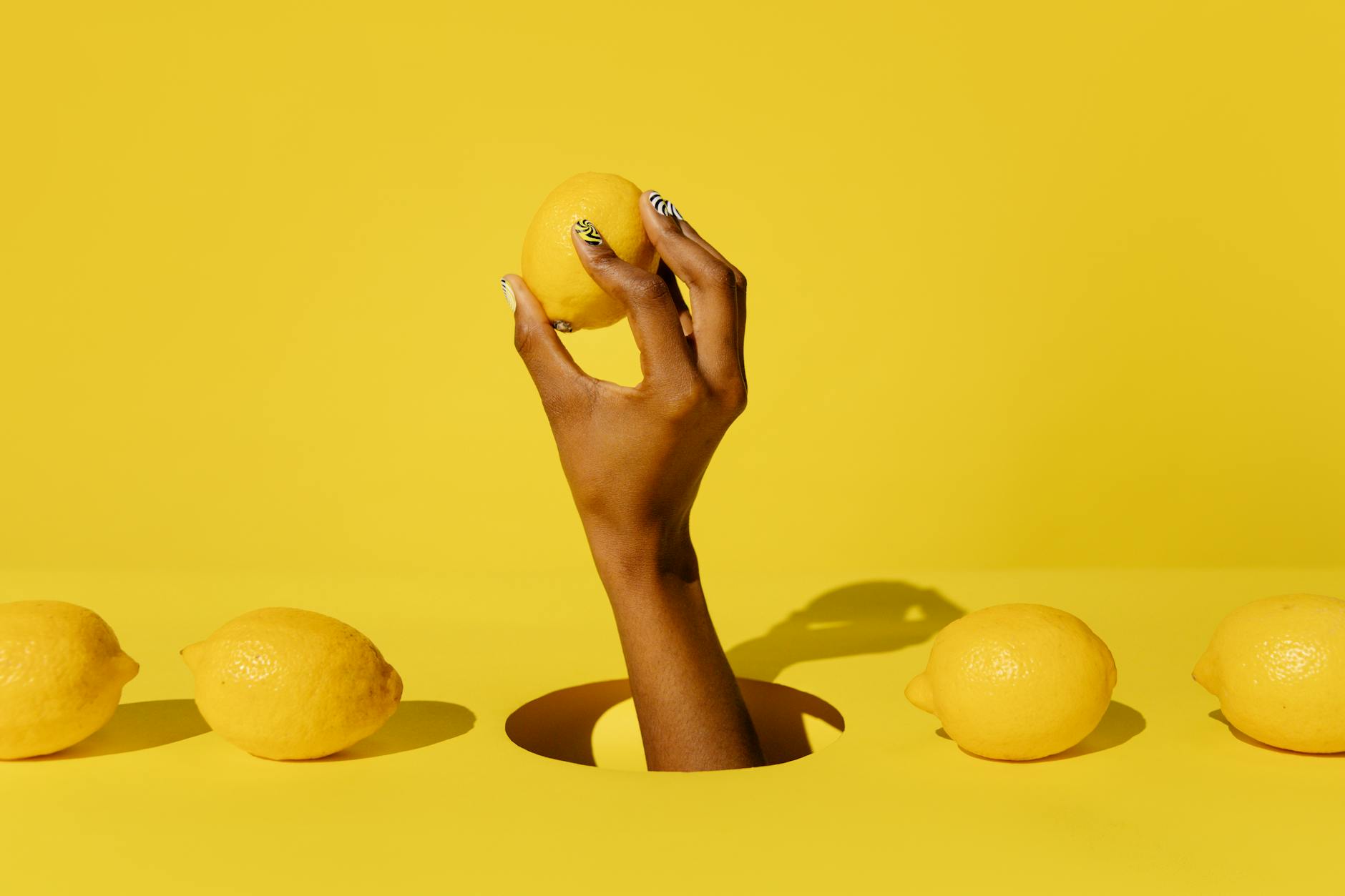 A hand holding a fresh lemon against a bright yellow background, representing natural, gentle stimulation.