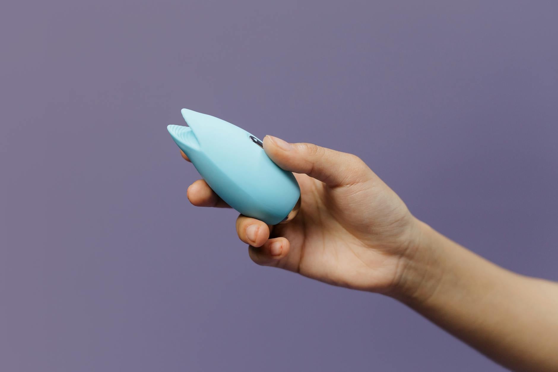 Woman holding a blue and pink vibrator thoughtfully against a purple background.