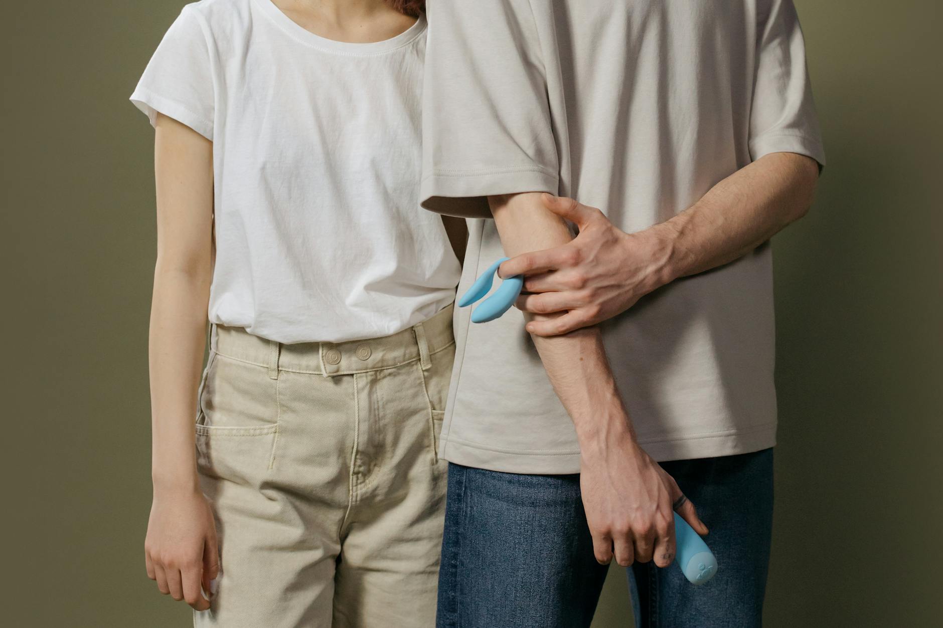 A young couple standing together indoors, holding a blue vibrator, symbolizing modern intimacy and reconnection