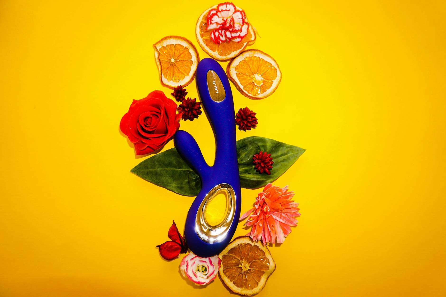 A lemon vibrator surrounded by fresh fruit and flowers on a bright yellow background